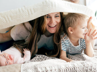 Happy mommy plays with the children on the bed and covers the children and herself with a blanket.