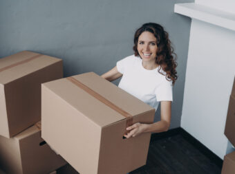 Joyful female homeowner standing in new house holding cardboard box. Moving, apartment renovation