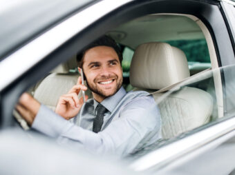 Young businessman with shirt, tie and smartphone sitting in car.